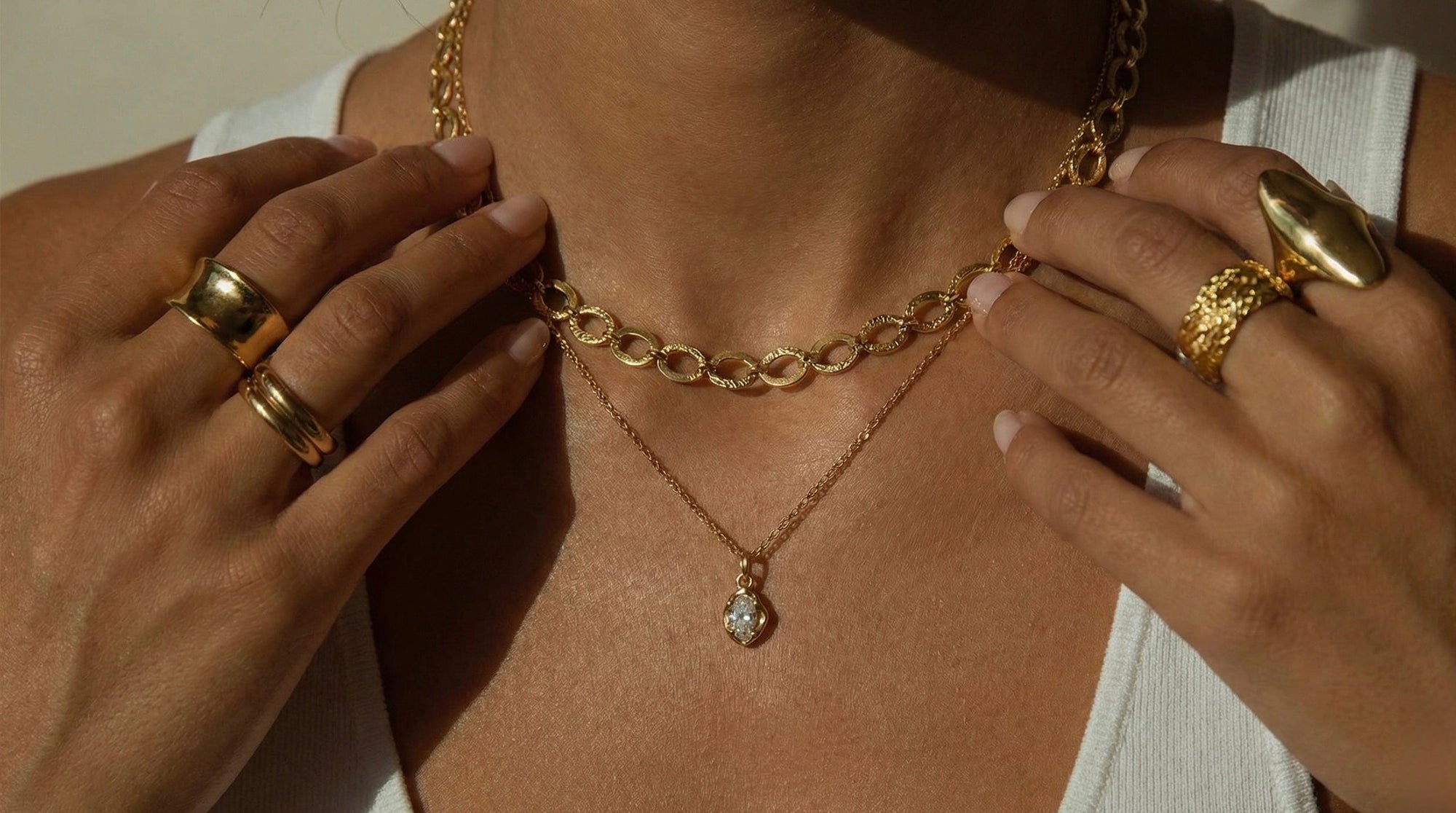 Gold necklace with a pendant worn by a person, with hands adjusting the necklace.