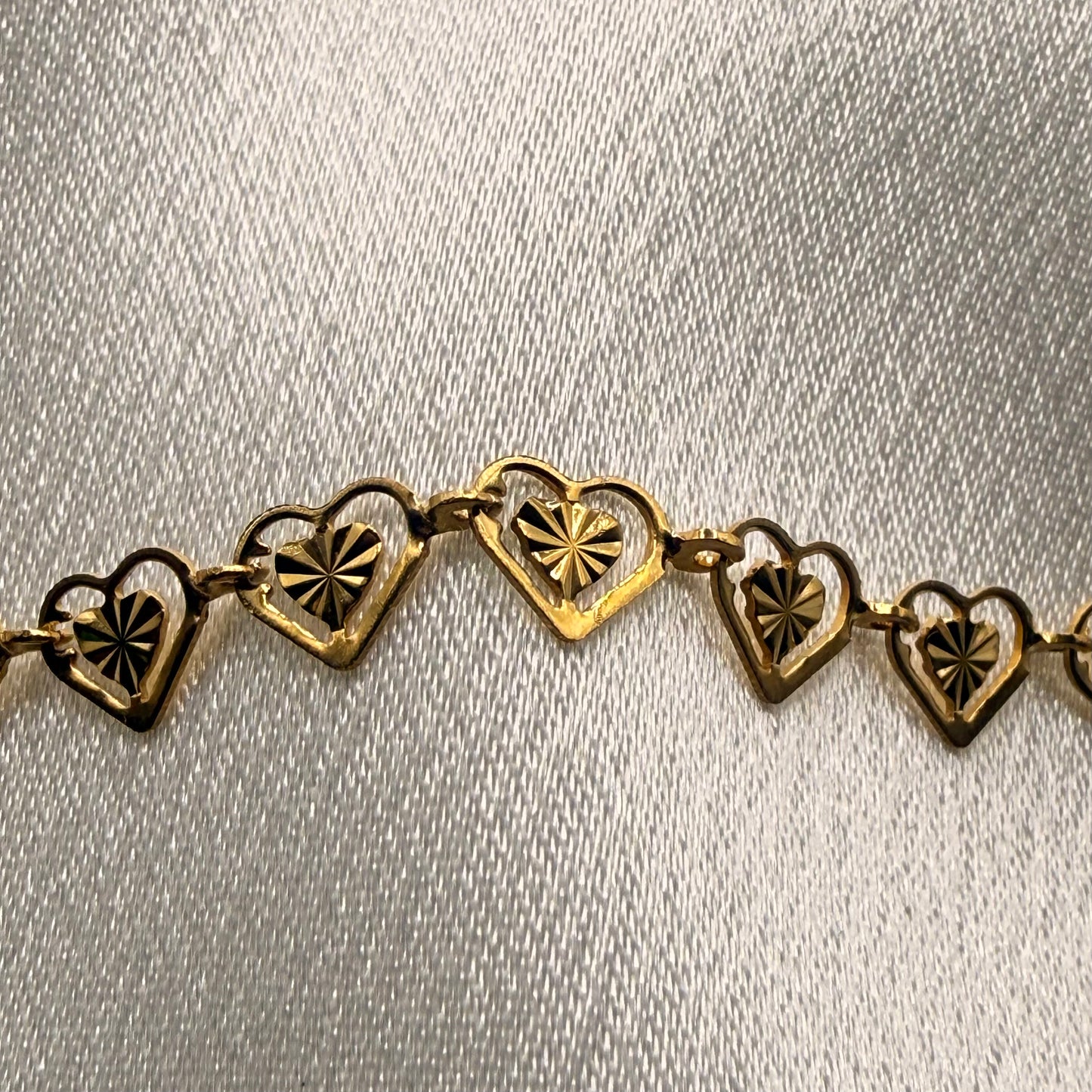 Gold necklace with heart-shaped links on a light gray background close up