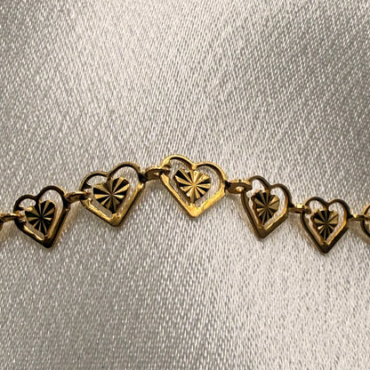 Gold necklace with heart-shaped links on a light gray background close up