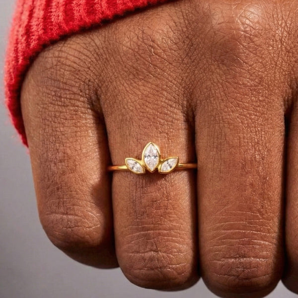 Gold ring with a diamond design on a person's finger against a gray background