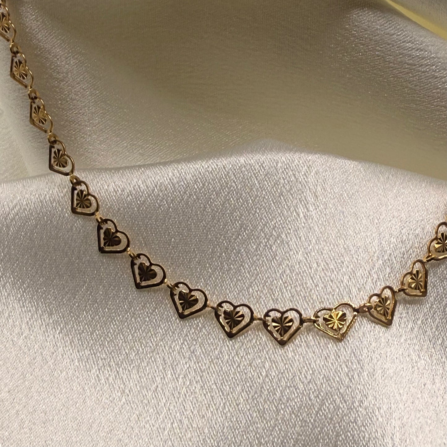 Gold necklace with heart-shaped pendants on a white fabric background